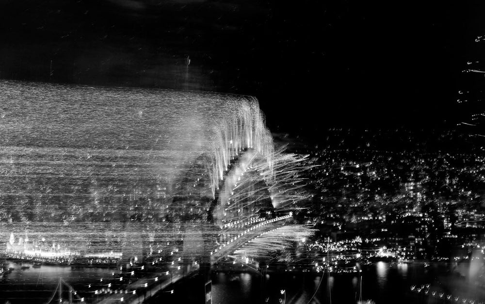 A blurred image of the Sydney Harbour Bridge with fireworks, likely taken from a distance or with a shaky camera.